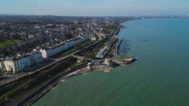 Aerial drone footage of Monkstown village coastline with Georgian terrace houses, coastal road, and calm Dublin Bay waters stretching toward the city horizon.
