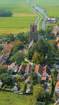 Aerial view of Ransdorp village in the Netherlands, showcasing traditional Dutch houses with red roofs, a prominent church tower, and lush green agricultural fields. A narrow canal winds through th...