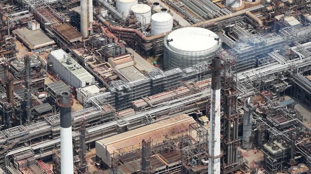 High angle perspective revealing the intricate network of pipelines, storage tanks, and smokestacks of a large industrial oil and gas refinery complex producing fossil fuels