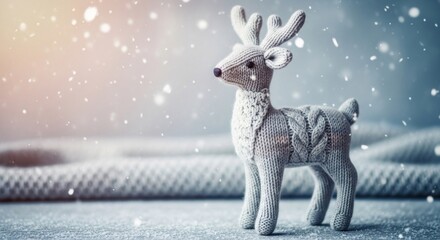Fototapeta premium A knitted reindeer figurine with a sweater stands on a snowy surface, surrounded by falling snowflakes.