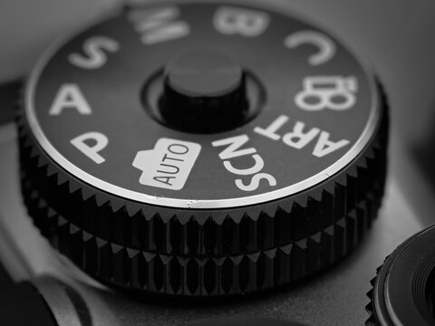 Macro close up of camera mode dial showing auto and scene settings with textured grip detail and warm lighting