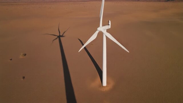 Desert Wind Turbines Casting Long Shadows Across Sand.