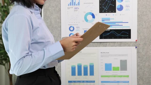 Asian businesswoman analyzing data and charts on a presentation board in office.