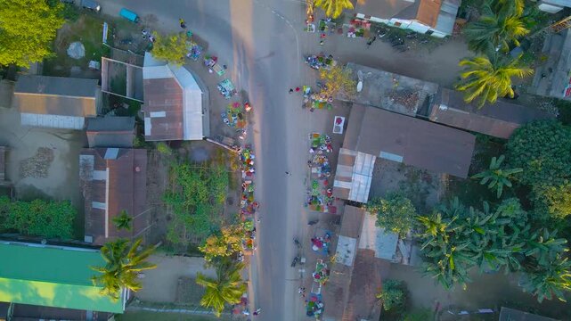 Drone view of busy village market with vendors, shops, umbrellas, and people in Byaskuchi, Assam.