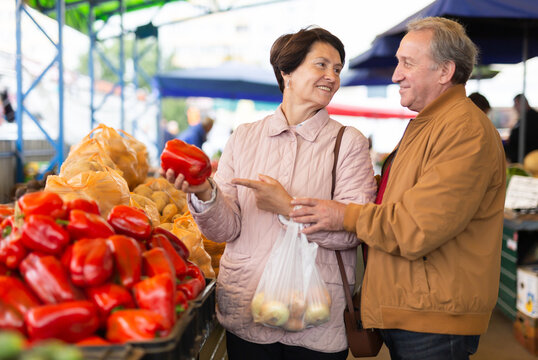 Aged man and woman customers buying pepper in open-air market