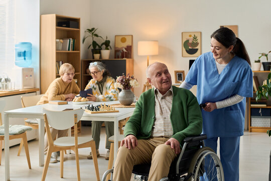 Senior man with disability sitting in wheelchair while young adult caregiver assisting in nursing home. Useful for elder care, assisted living, rehabilitation, healthcare support marketing