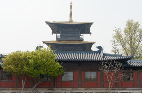 A traditional pagoda-style temple with layered tiled roofs and wooden facade framed by leafy and bare trees, evoking heritage, tranquility and architectural detail for travel, culture and history