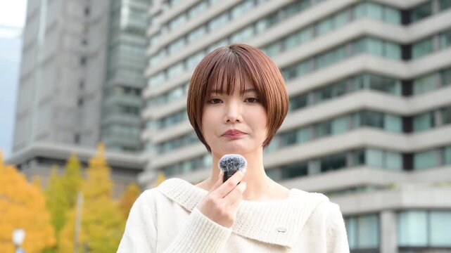 ビル前でピンマイクを使って話す日本人女性