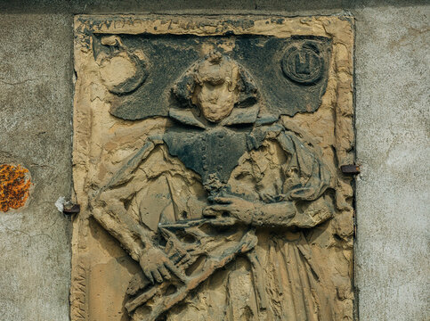 Seventeenth-century female figure epitaph without face carved in stone on church facade, Europe