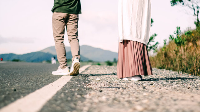 Close up legs of a couple walking on the side of a rural road with mountain background.