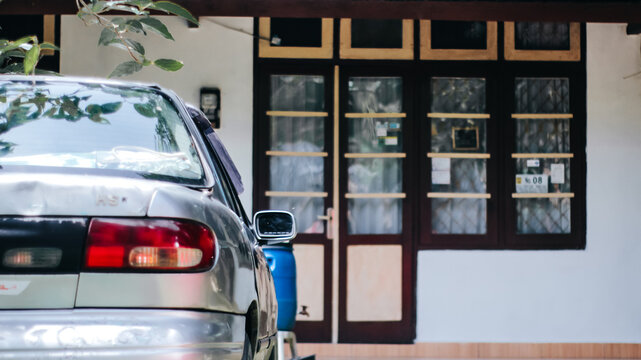 Old silver sedan car parked in front of a classic house with wooden windows.