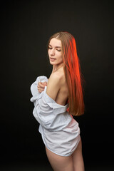 A young woman poses in a white off-the-shoulder shirt on a black background. The soft lighting highlights her relaxed and confident expression. She is wearing minimal underwear, which adds to her sens © SergeiPh