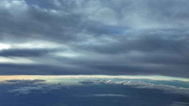 Pilot view from the cockpit of a jet airplane while flying under and endless layer of stratus clouds at sunset with a golden color horizon.