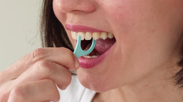 Young Woman Using Blue Plastic Dental Floss Pick on White Healthy Teeth &mdash; Female Interdental Cleaning with Disposable Flosser, Oral Hygiene Daily Routine, Gum Care and Preventive Dentistry