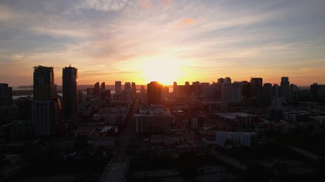 Drone pulling back from downtown San Diego at 7PM with sunlight reflecting off buildings during golden hour.