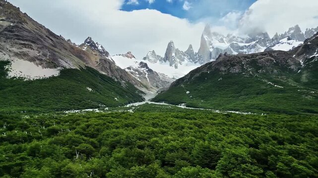 Fitz roy mountain range in argentinian patagonia with lush green forest below under cloudy skies.