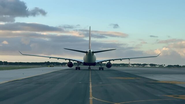 Pilot view of the rear part of a masive twin-engine wide-body jet taxiing along an airport taxiway at sunrise. Shot taken from a jet taxiing behind.