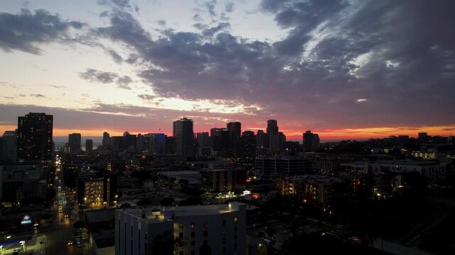 Drone pulling back from downtown San Diego skyline at 8PM revealing a colorful sunset sky and expansive city view.
