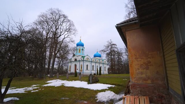Blue-domed Christ Transfiguration Orthodox Church in Cēsis, Latvia, with patchy late-winter snow in the park grounds.