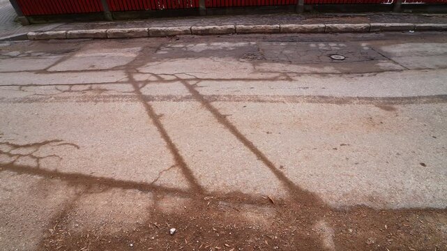 Patched asphalt street with branching cracks, gritty sand bands and curb edge&mdash;post-winter thaw road damage and municipal maintenance concept.