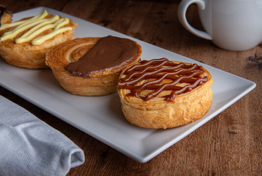 Reposteria casera, pan de hojaldre sobre un plato blanco para disfrutar en familia con cafe o leche, relleno y cubierto de cajeta con servilleta al lado.