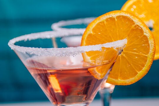 Close-up of a pink cocktail in a sugar-rimmed martini glass garnished with an orange slice. Elegant drink photography for bar or menu use.