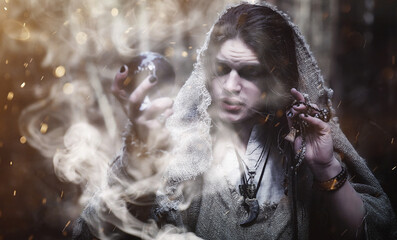 Fototapeta premium Fairy magician. A sorcerer with a glass sphere, a magical spell and a ritual. Elder with a staff and a cross in the forest. Black and white magic. A spell in an old book.