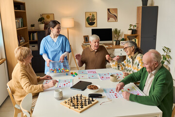 Senior group playing cognitive games with female caregiver in care home, supporting memory training and social engagement. Ideal for eldercare, dementia support, senior wellness marketing © pressmaster