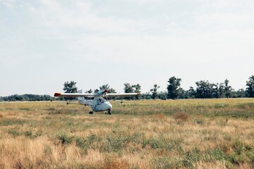 Fototapeta premium crop duster airplane rolling on dirt runway in open farmland landscape under sunlight with empty space for text panoramic banner scene, agribusiness, aviation, rural economy