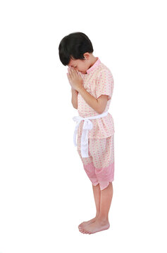 Charming young Asian boy dressed in traditional pink Thai costume performing the "Wai," a respectful Thai greeting gesture, while standing against white background. Side view.