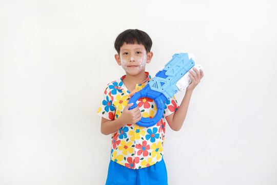 A young Thai boy, with face powder for the Songkran festival, is smiling and holding colorful water gun against white background.