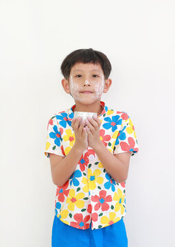 Thai boy, with white facial powder applied for Songkran festival and wearing colorful floral shirt, is standing and holding a small silver bowl, getting ready to splash water.