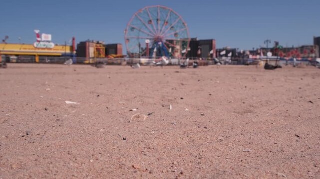 Coney Island sandy beach in Brooklyn, New York, United States. Boardwalk near retro luna park. Ferris wheel in american amusement park on ocean coast. Waterfront summer holiday promenade in NYC, USA.