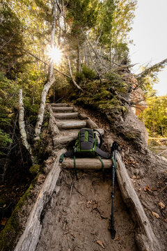 Hiker's backpack and trekking poles resting on forest trail steps