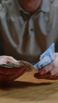 Close up vertical: man trader or businessman counts salary usd banknotes at home, hands. Male entrepreneur holds stack of dollar bills in palms, keeps money records, budget. Counting american paper