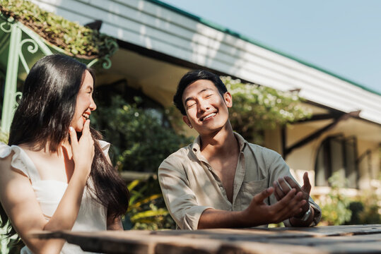 A cheerful young Asian couple flirting and laughing together while sharing stories. Outdoor shot.
