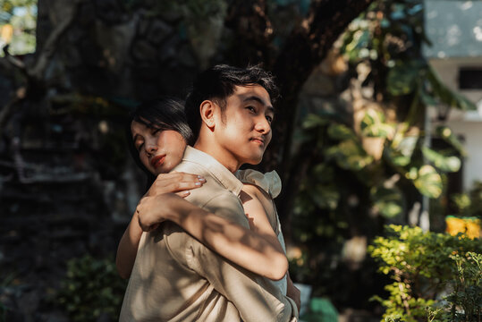 A proud young Asian man receiving a warm hug from his female best friend as their bond deepens into a new romantic relationship. Outdoor shot.