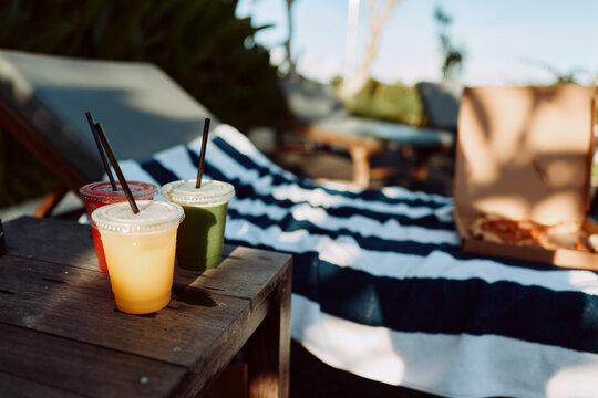 Outdoors picnic scene with a wooden table, colorful drinks, a striped blanket, and warm sun, capturing casual relaxation and a bright summer lifestyle in a simple, candid moment.