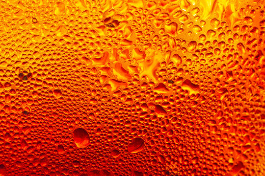 A close-up image of a cold cola with condensation on a glass background,Macro shot of a refreshing amber-colored drink with ice cubes, showing heavy water condensation droplets on the outside.