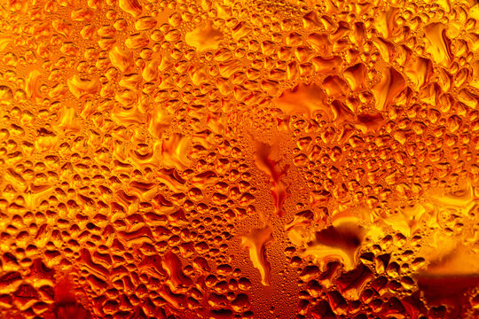 A close-up image of a cold cola with condensation on a glass background,Macro shot of a refreshing amber-colored drink with ice cubes, showing heavy water condensation droplets on the outside.