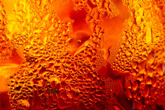 A close-up image of a cold cola with condensation on a glass background,Macro shot of a refreshing amber-colored drink with ice cubes, showing heavy water condensation droplets on the outside.