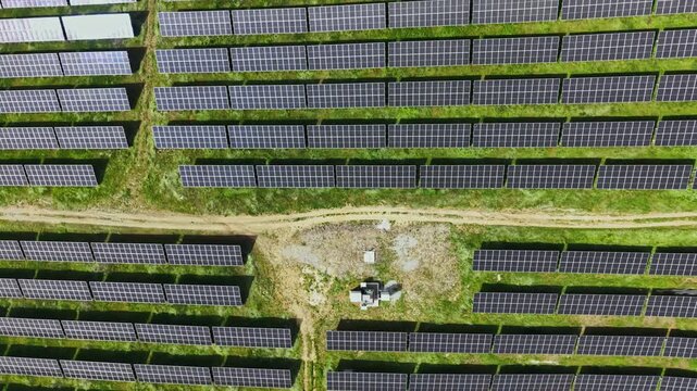 Multiple rows of solar panels stretch across the ground in a field. A small maintenance area is visible in the center. This scene shows a renewable energy initiative in action.