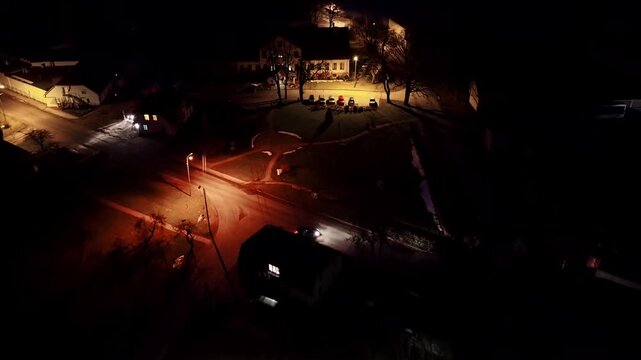 Lone car driving down the rural village road turns right in night aerial view