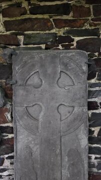 Ancient Manx cross stone tablet with carved circular motifs set against a stone wall. vertical video, push forward