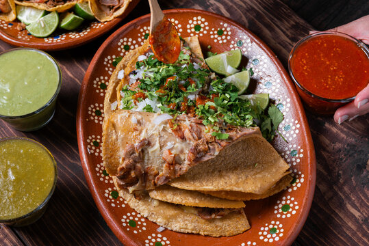 Close-up of a hand adding red sauce to a delicious gringa al pastor on a decorated plate