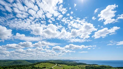 Breathtaking wide-angle panoramic view of rolling green hills overlooking the deep blue ocean under a vast sky filled with fluffy white clouds © Oktafianto