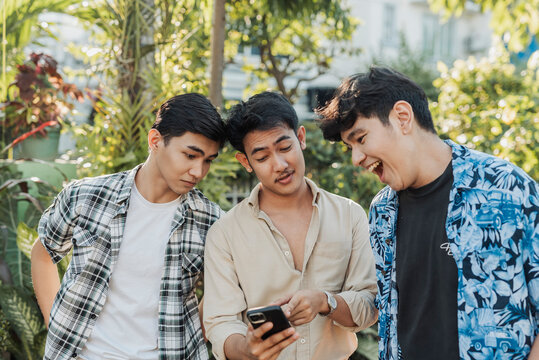 A excited young Asian men reacting while checking a woman&rsquo;s social media profile together on a smartphone during a casual outdoor hangout. Outdoor shot.