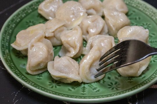 a fork pressing into a steaming hot meat dumpling (pelmeni) on a green patterned ceramic plate,