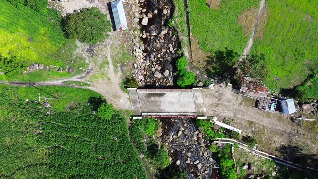 Top-down aerial drone footage of a rural concrete bridge crossing a rocky river stream