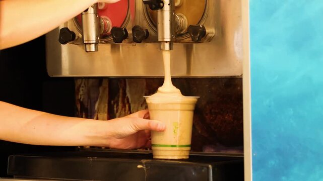 Barista filling plastic cup with refreshing iced coffee slushy from dispenser machine in cafe.